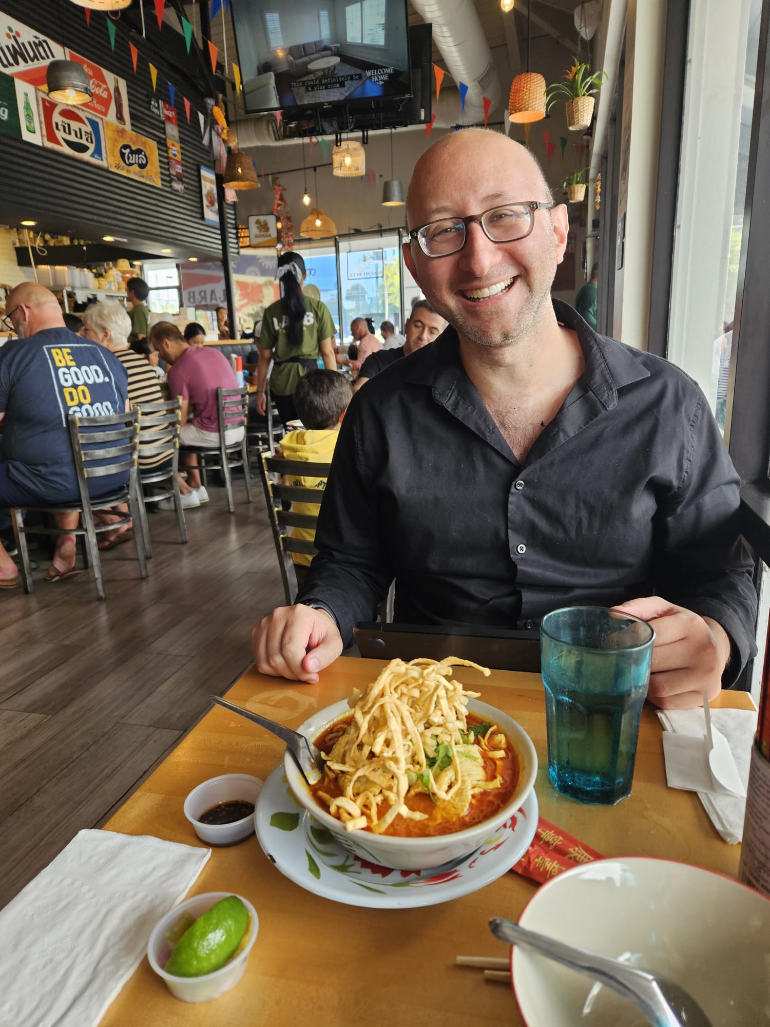 David grinning at a Thai restaurant table behind a bowl of khao soi, April 6, 2025